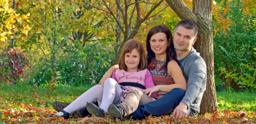 Family sitting on the ground in a park during autumn, surrounded by colorful trees and fallen leaves